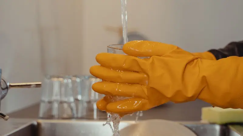 Handen met schoonmaakhandschoenen die de spoelbak en vaatwasseronderdelen reinigen